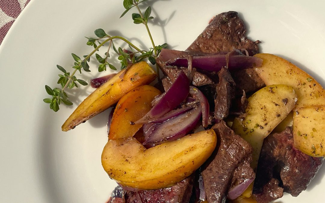 Geröstete Leber mit Apfelspalten und roten Zwiebeln angerichtet auf einem weißen Teller, dekoriert mit einem Thymianzweig