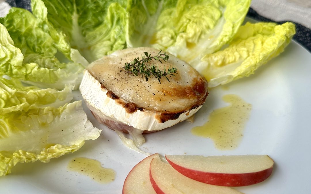 Braun angekrusteter Ziegenkäse-Apfelring, mit Thymian dekoriert auf einem weißen Teller, umgeben von Salatblättern und Apfelspaltendekoration.
